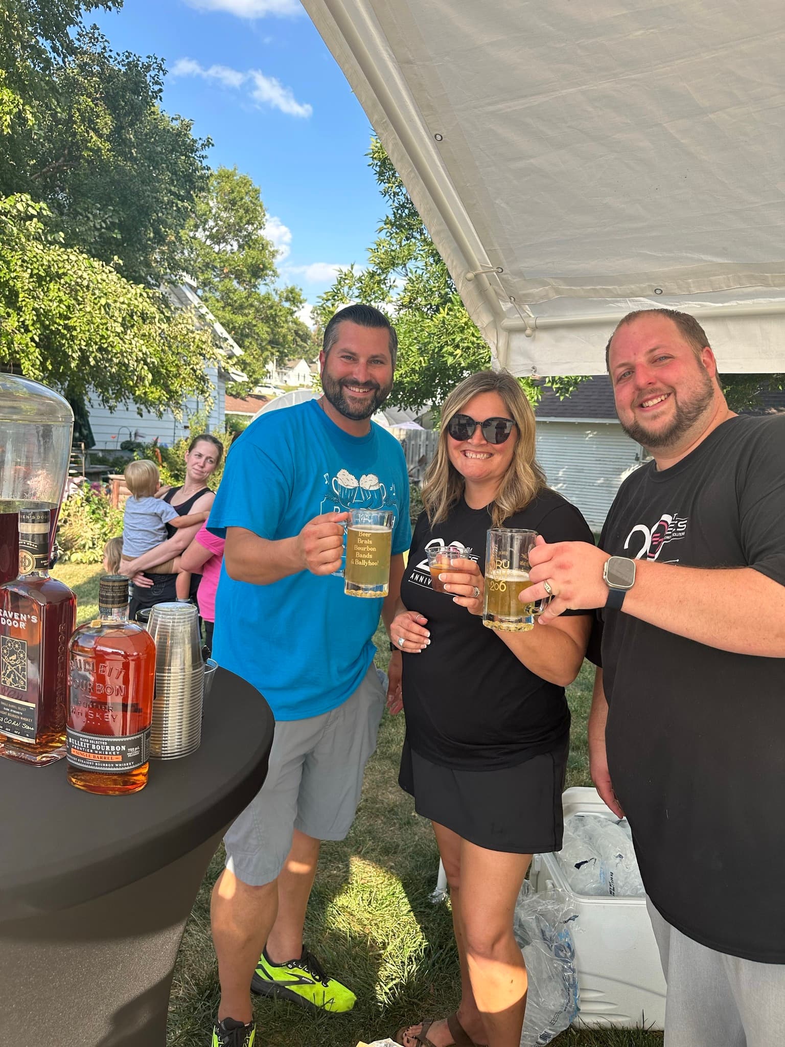 Three guests raising BruBash steins at the bourbon table under the tent